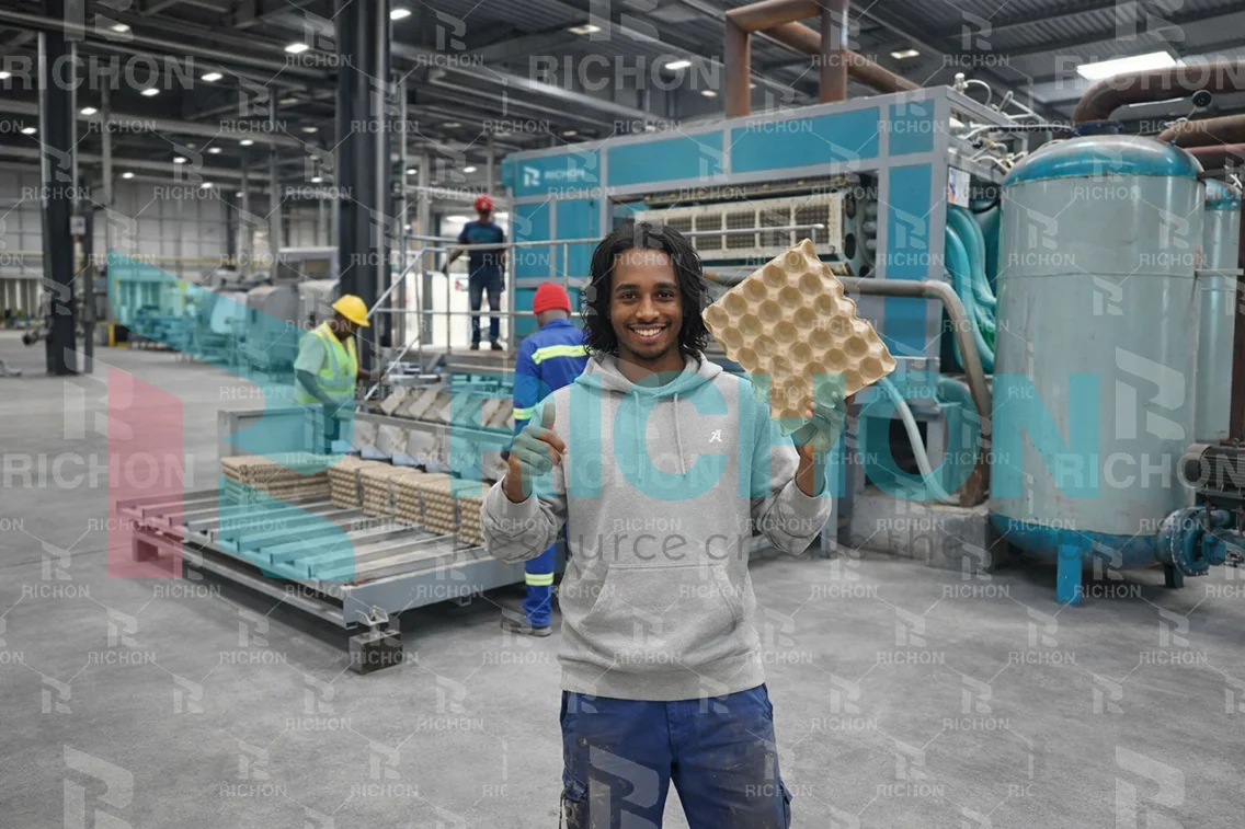 Egg tray production worker holding finished pulp molded trays in modern industrial factory with forming machine and drying system